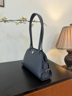 Blue top-handle handbag on side angle with small round snap and short curved strap