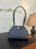 Blue top-handle handbag with structured shape, round snap button, and short side tabs