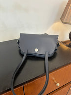 Blue top-handle handbag with front flap and round snap button, showing long shoulder strap