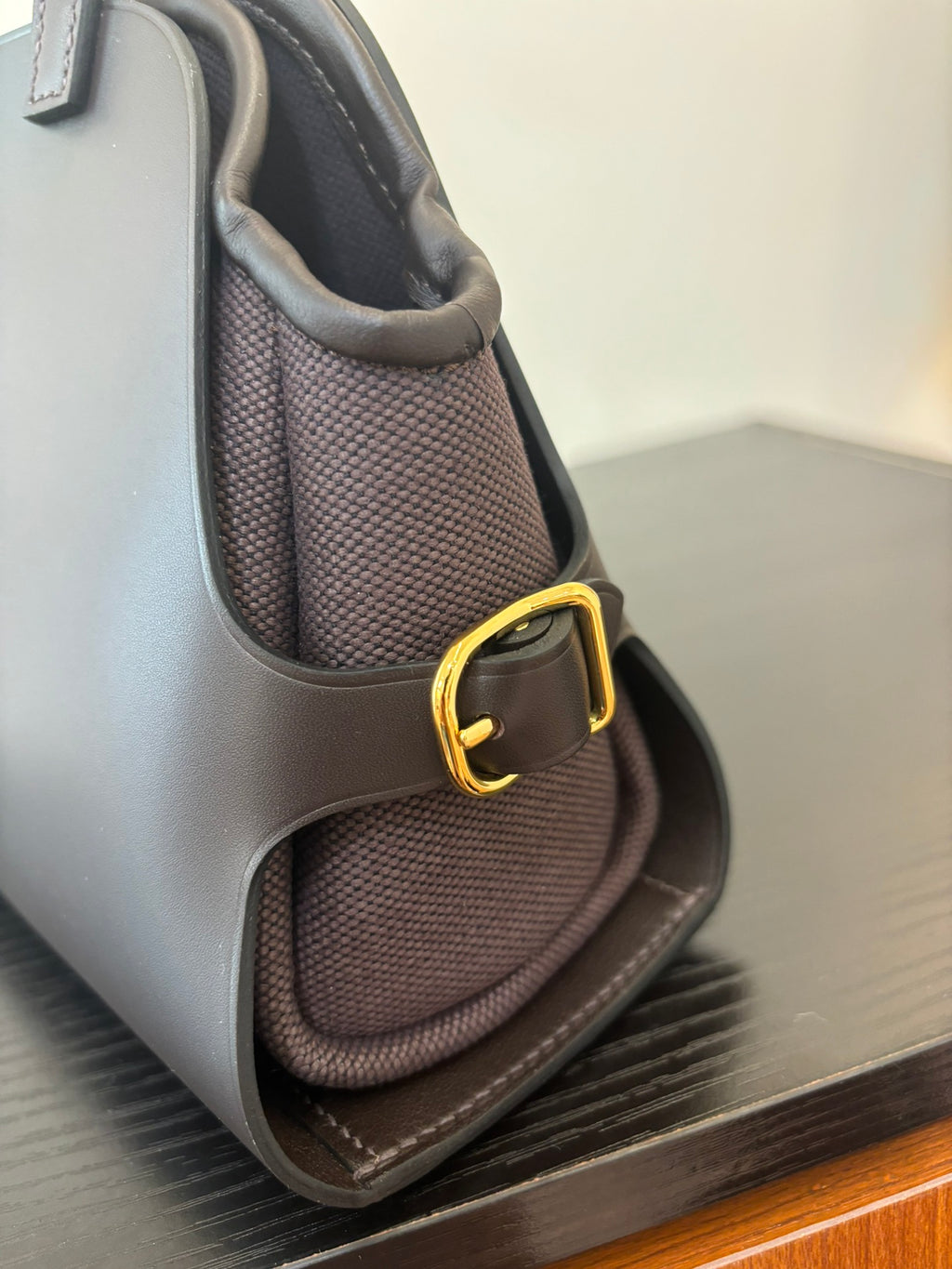 Hermes bag corner view with structured dark fabric, woven texture insert and gold-tone strap ring.
