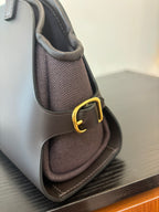 Hermes bag corner view with structured dark fabric, woven texture insert and gold-tone strap ring.