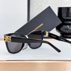 Balenciaga sunglasses with dark lenses, black frame, and gold B bar detail on temple