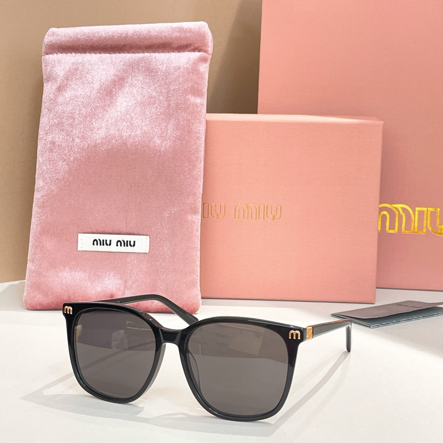 MiuMiu sunglasses with black frame and dark gray lenses, with pink storage pouch