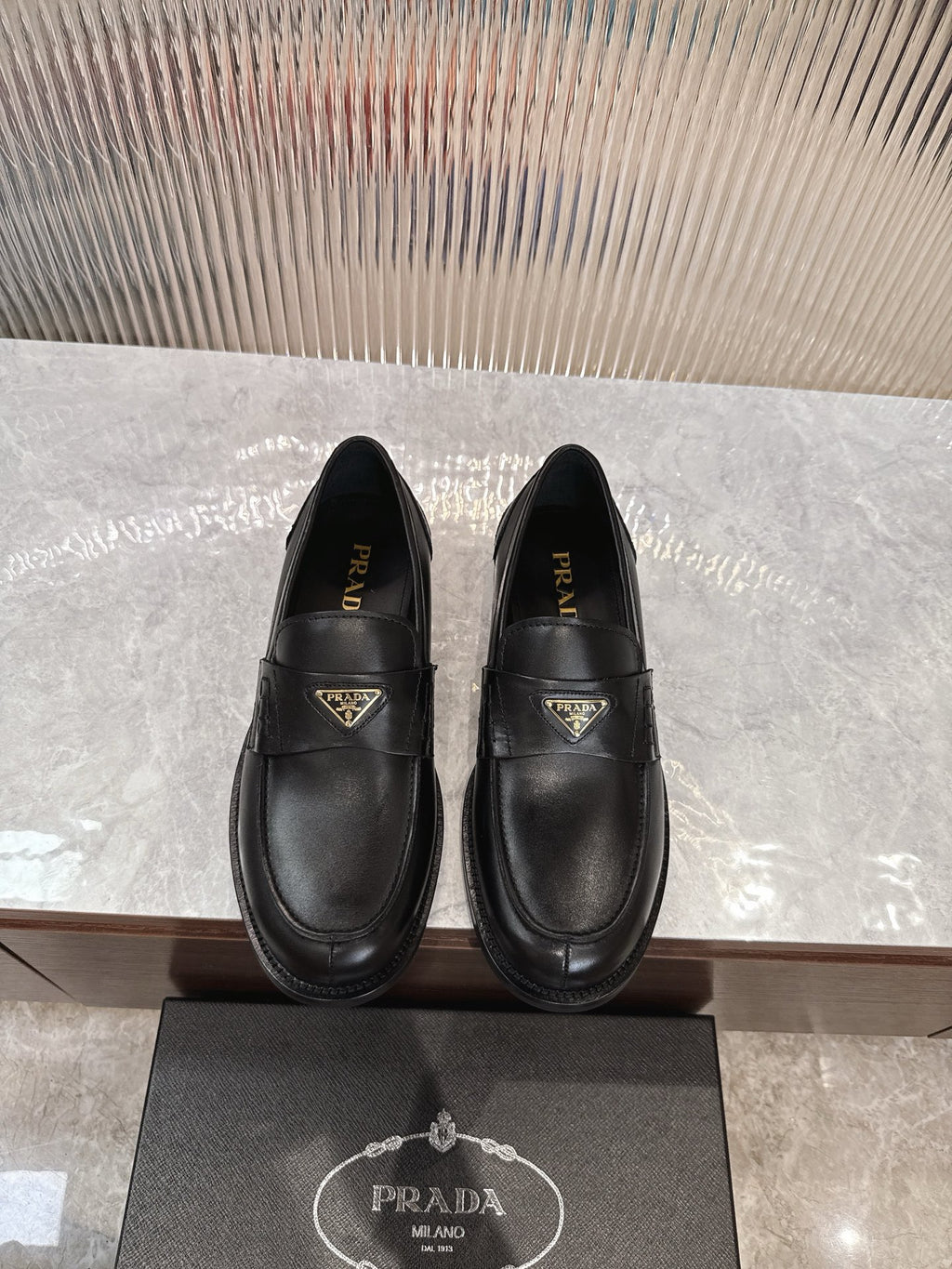 Prada black leather loafer with gold-trimmed triangular logo plaque, slip-on style