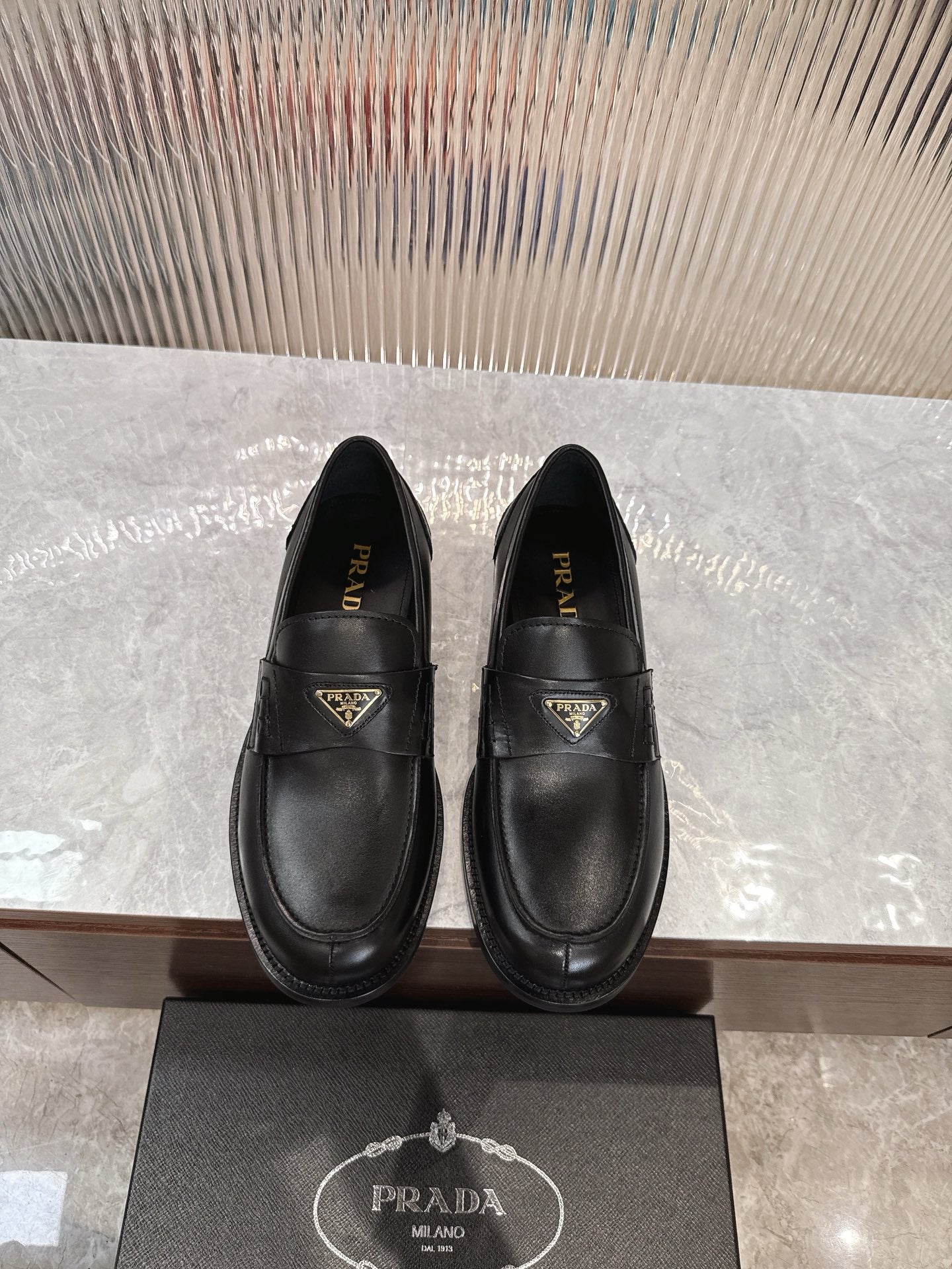 Prada black leather loafer with gold-trimmed triangular logo plaque, slip-on style
