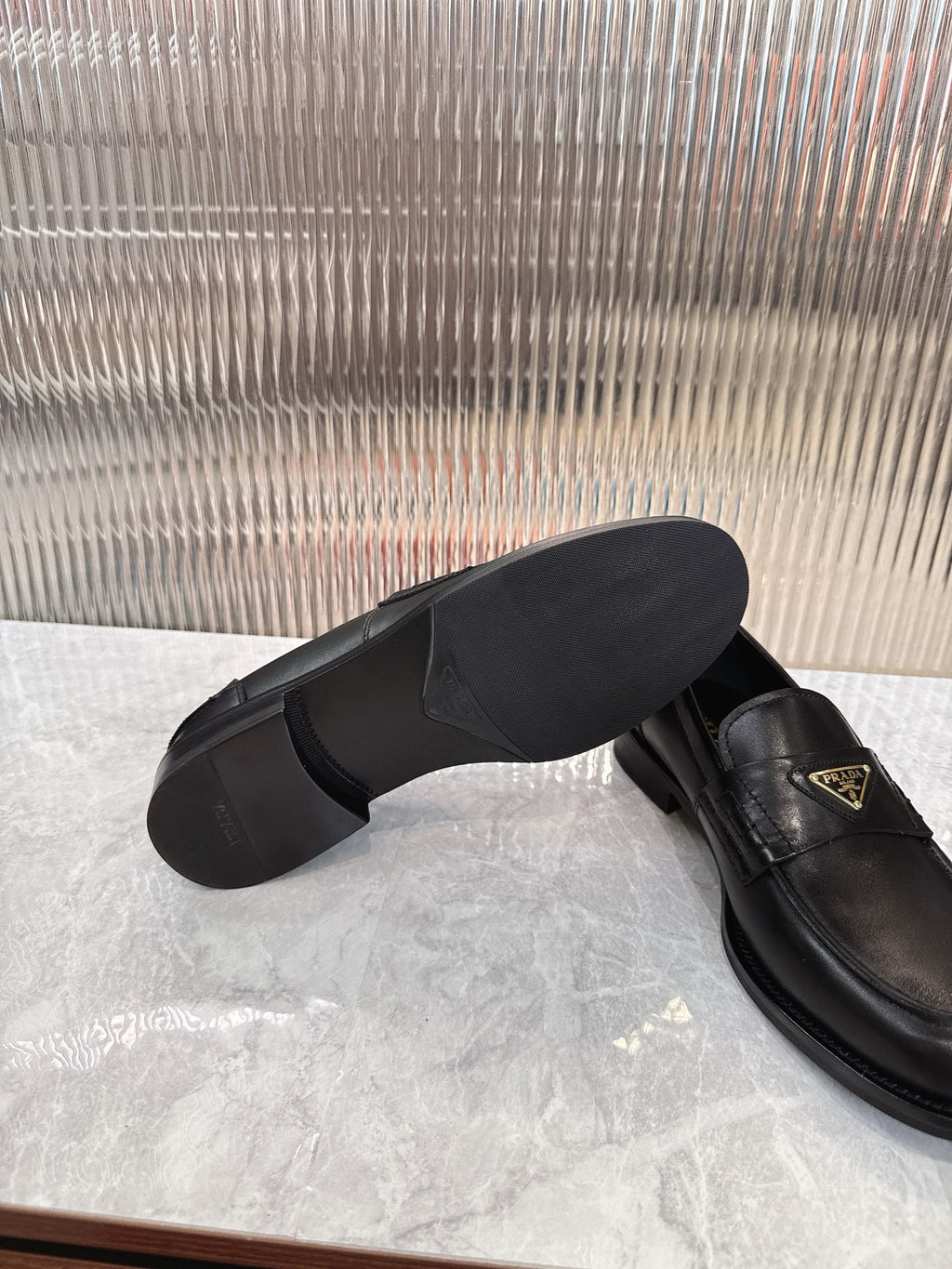 Prada black leather loafer with visible sole and gold triangular logo plaque, side view