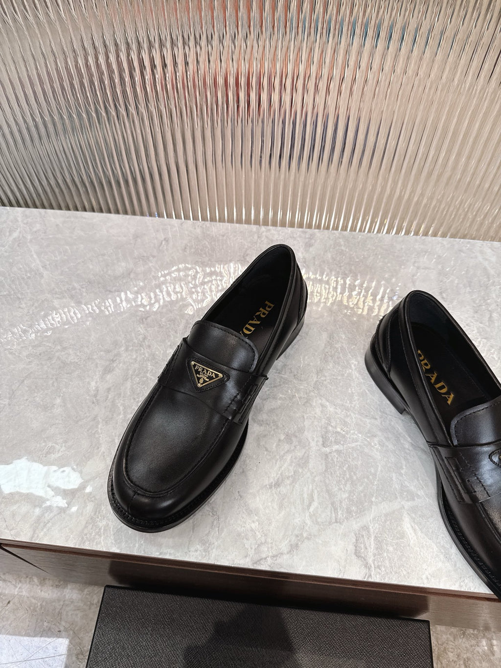 Prada black leather loafer with gold triangular logo plaque, angled side view