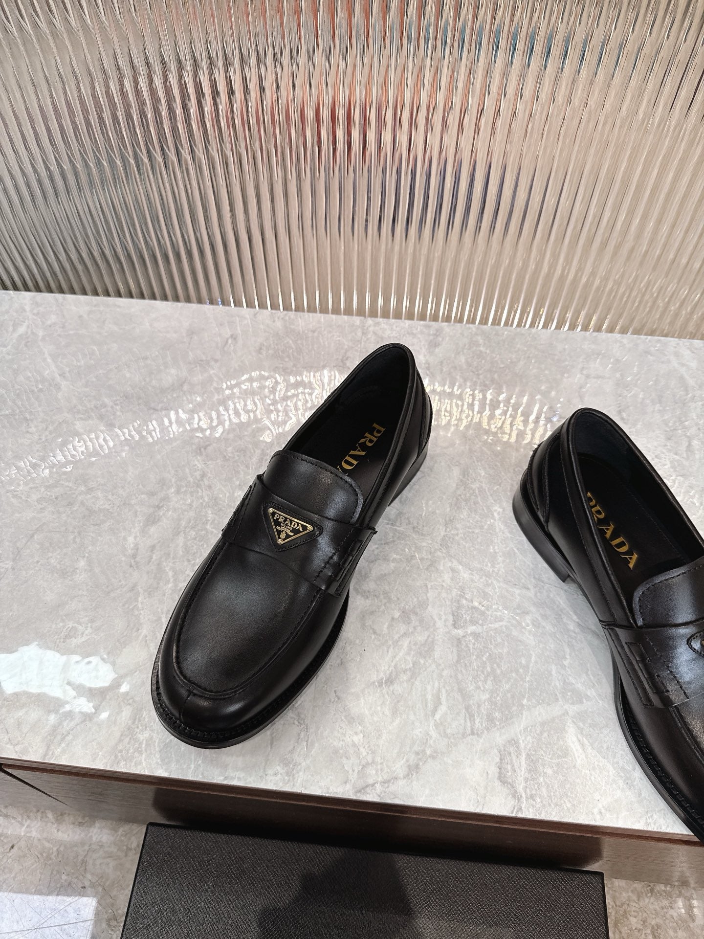 Prada black leather loafer with gold triangular logo plaque, angled side view