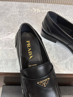 Prada black leather loafer close-up with gold triangular logo plaque