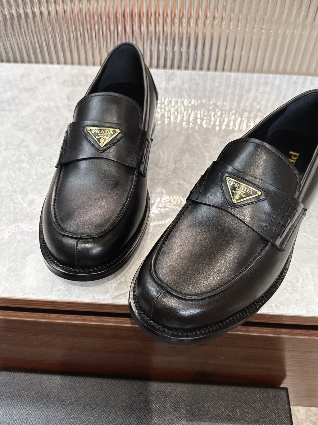 Prada black leather loafers with gold triangular logo plaques, front view
