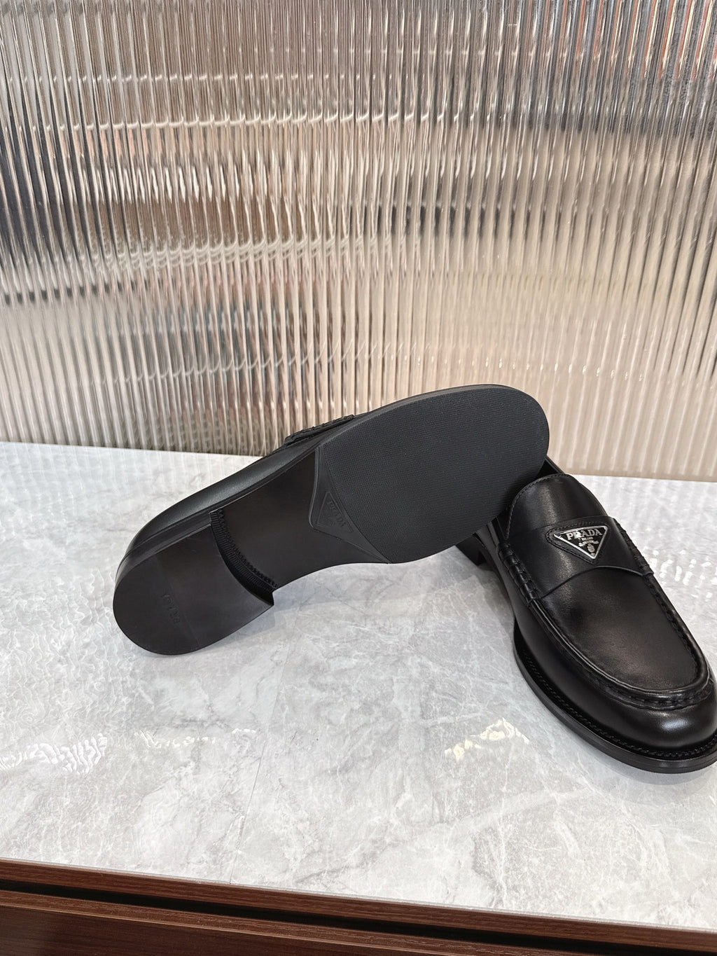 Black leather loafer, outsole and side angle with triangular logo detail on upper.