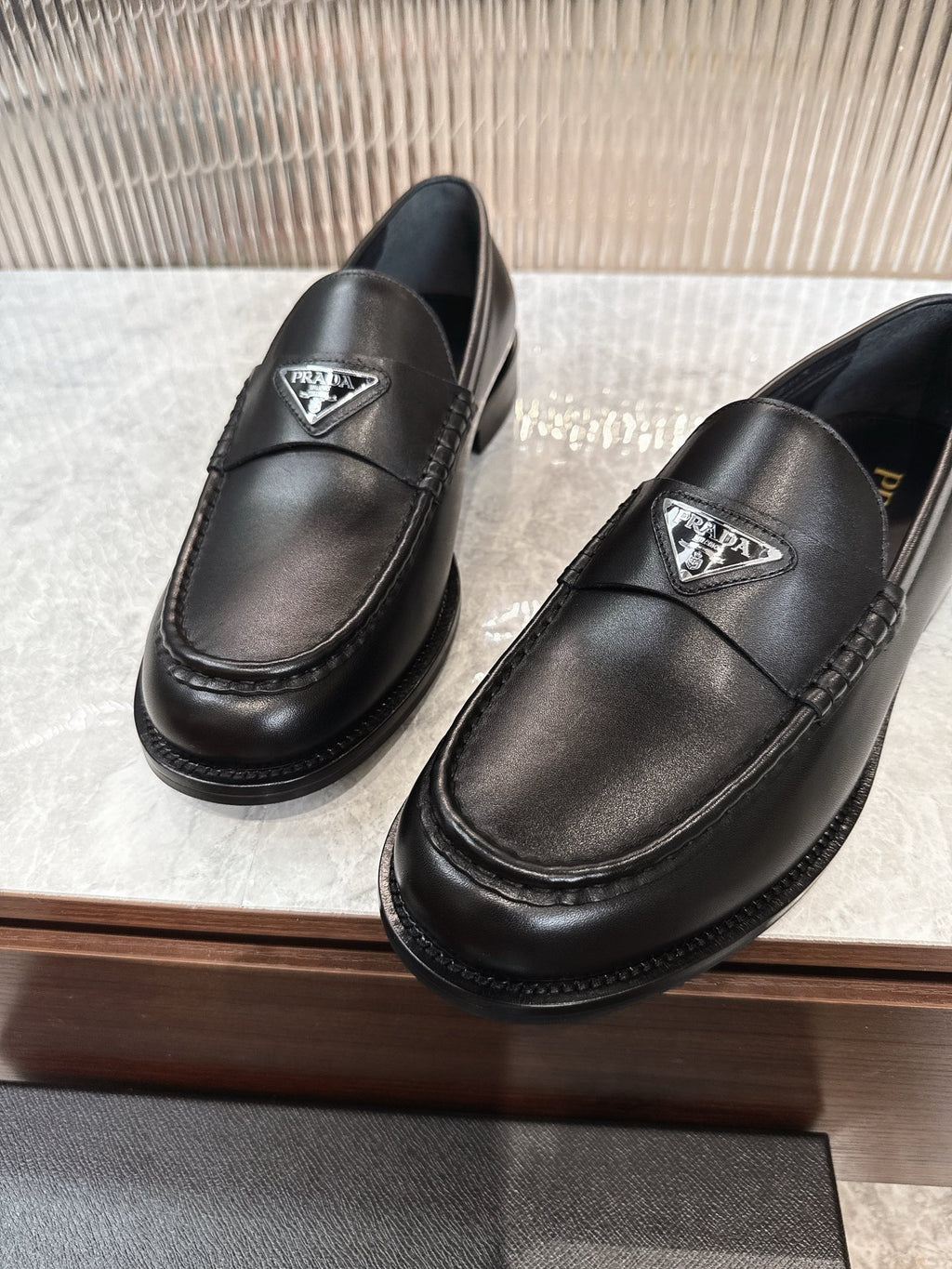 Black leather loafers with triangular Prada emblem; detailed stitching around the apron toe.