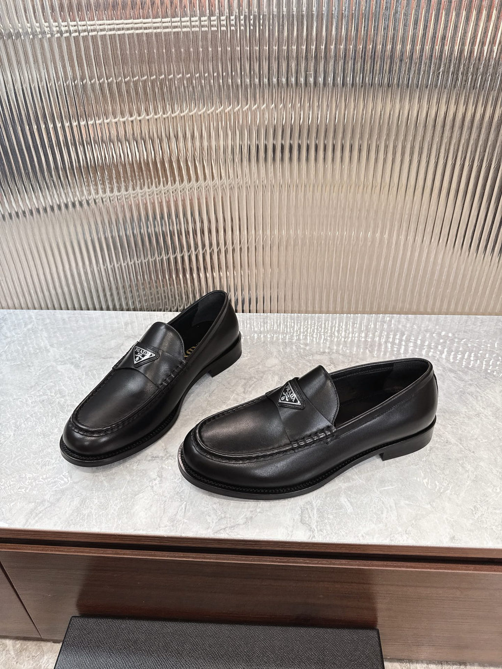 Prada unisex black leather loafers, pair on display with metal triangle badge