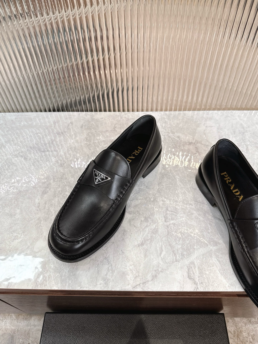 Black leather slip-on loafers with triangular logo on the vamp and stitched apron toe.