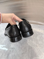 Black Prada unisex loafers, heel and back view held by hand, side panels visible.