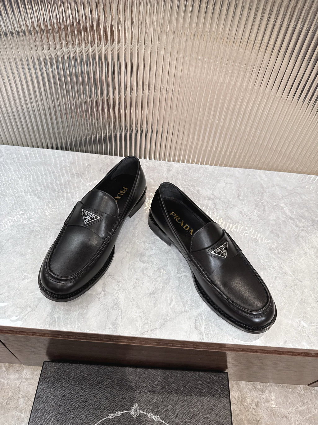 Black Prada unisex loafers, side view showing stitched detail and logo badge.
