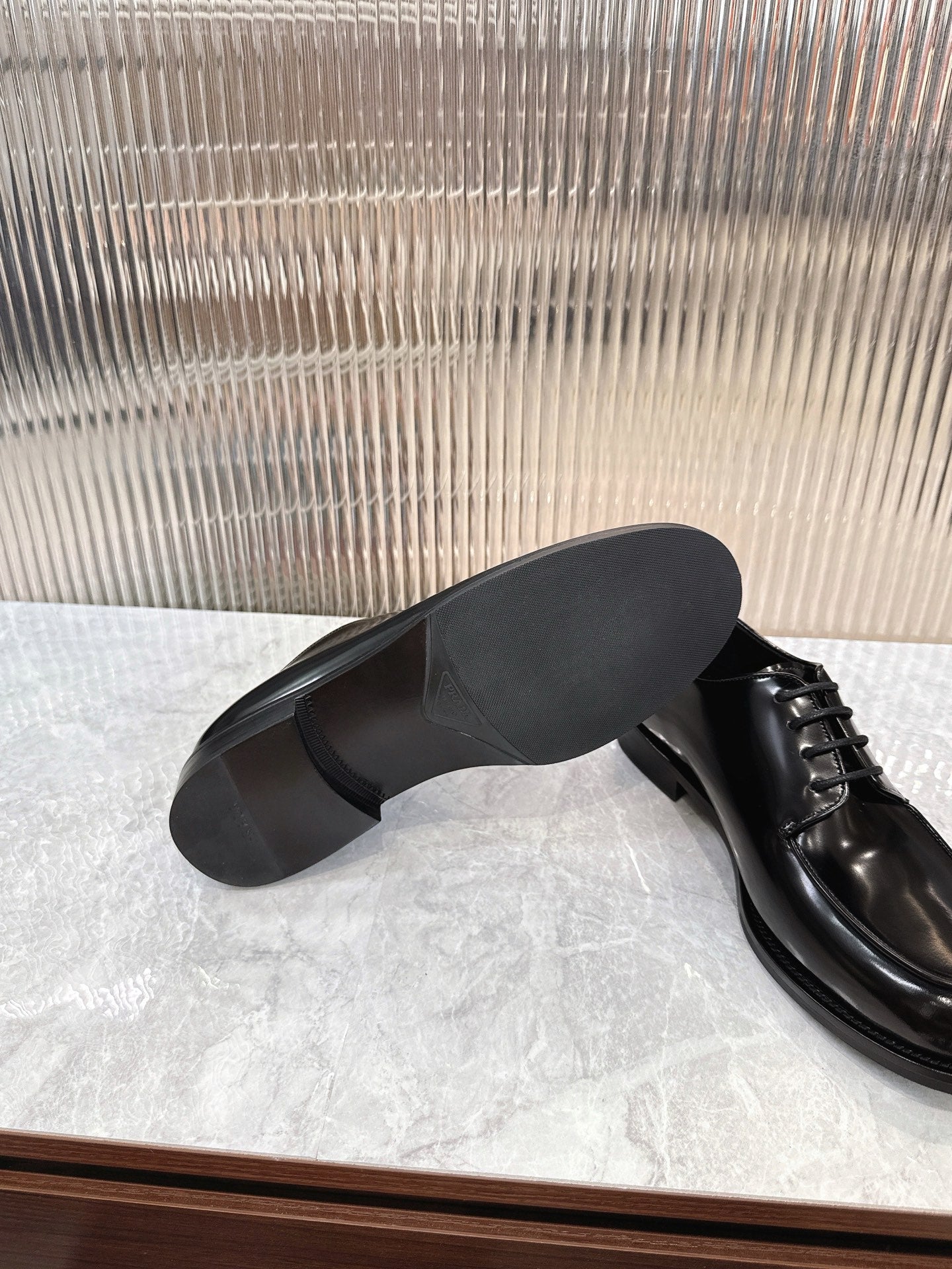 Prada unisex lace-up shoes, glossy black leather, visible underside of heel.