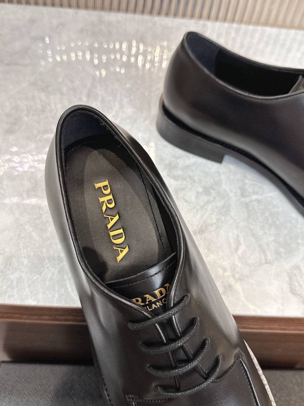 Black leather lace-up shoe showing interior Prada branding and laces