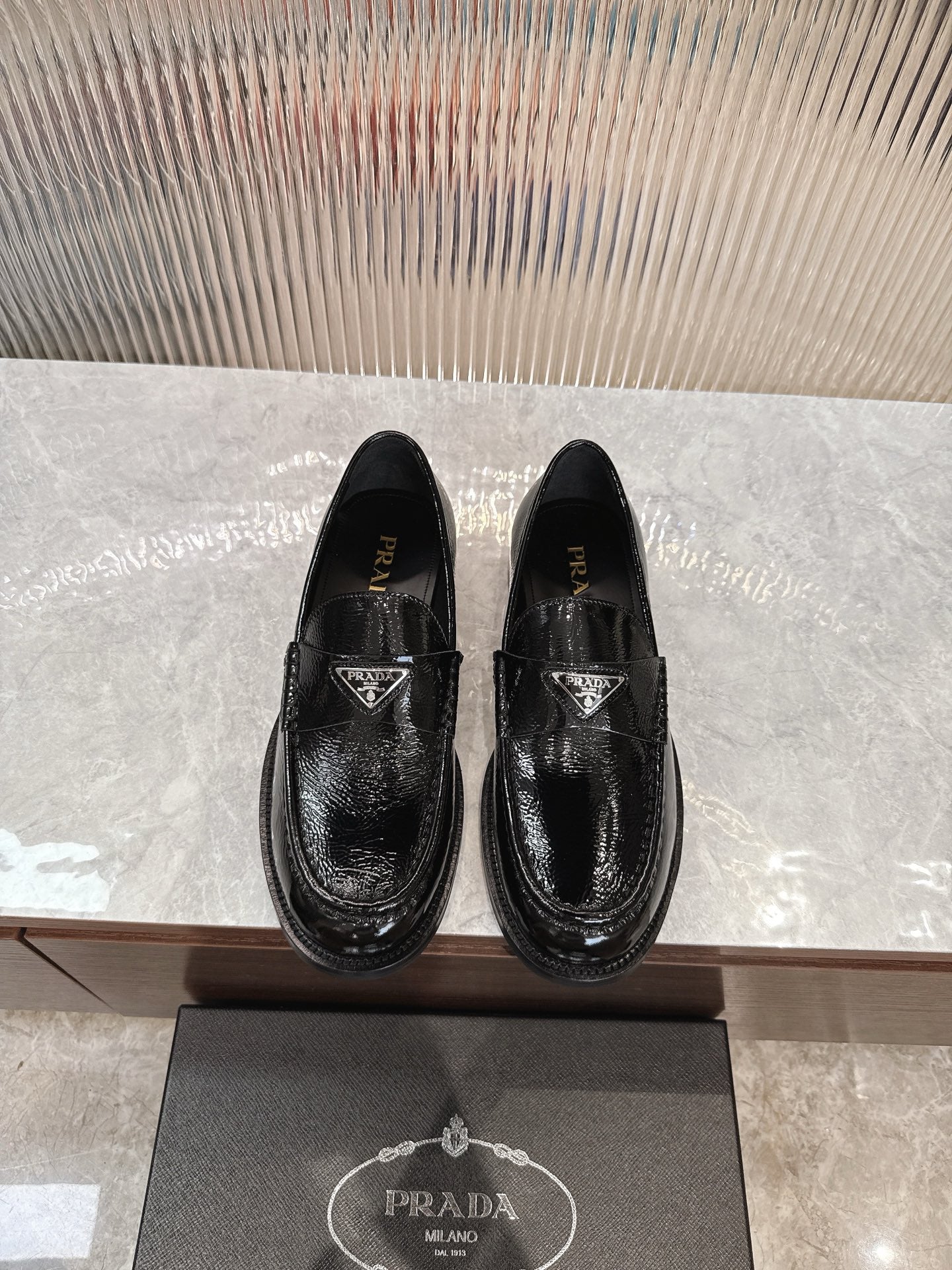 Black glossy leather loafers with Prada logo at vamp, slip-on style.