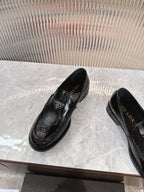 Black patent loafers with Prada badge on the strap, angled front view.