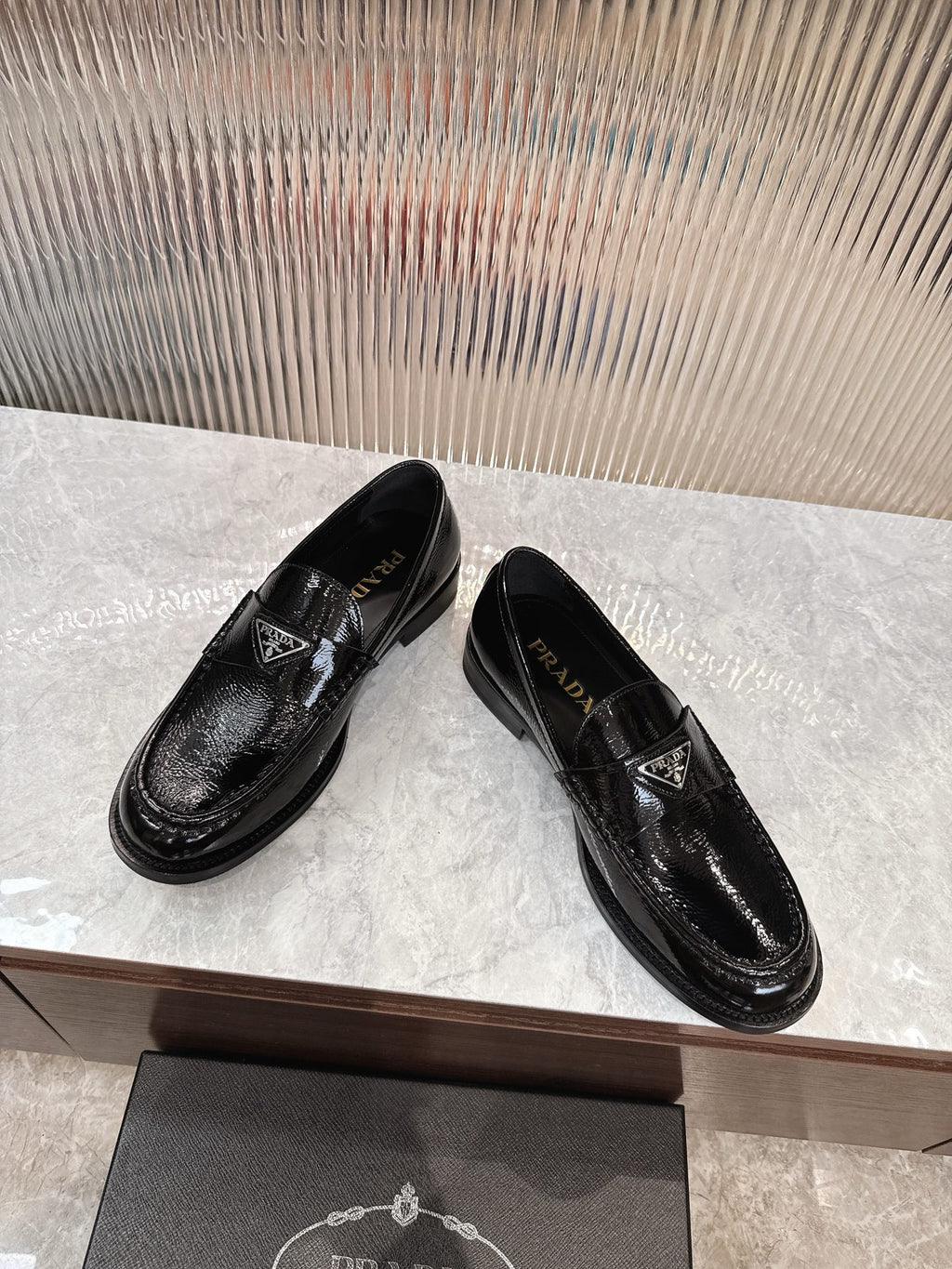 Pair of black patent loafers with decorative strap and Prada emblem, side view.
