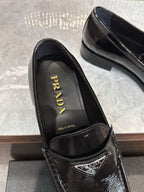 Black patent loafers with 'Prada' logo on insole and stamped crest detail.