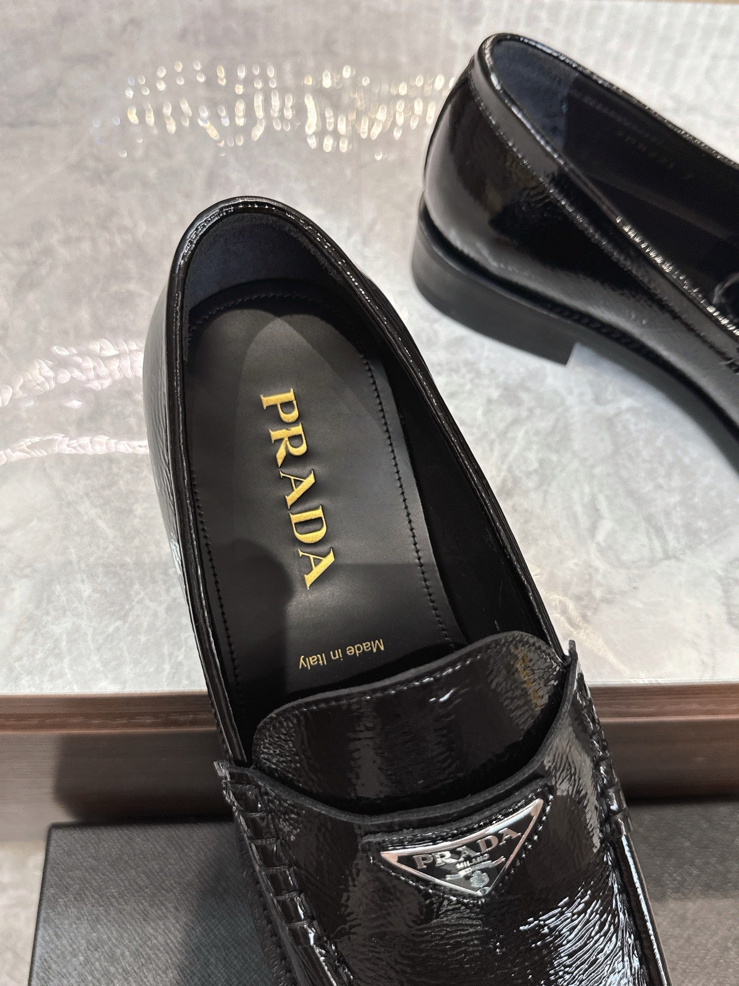 Black patent loafers with 'Prada' logo on insole and stamped crest detail.