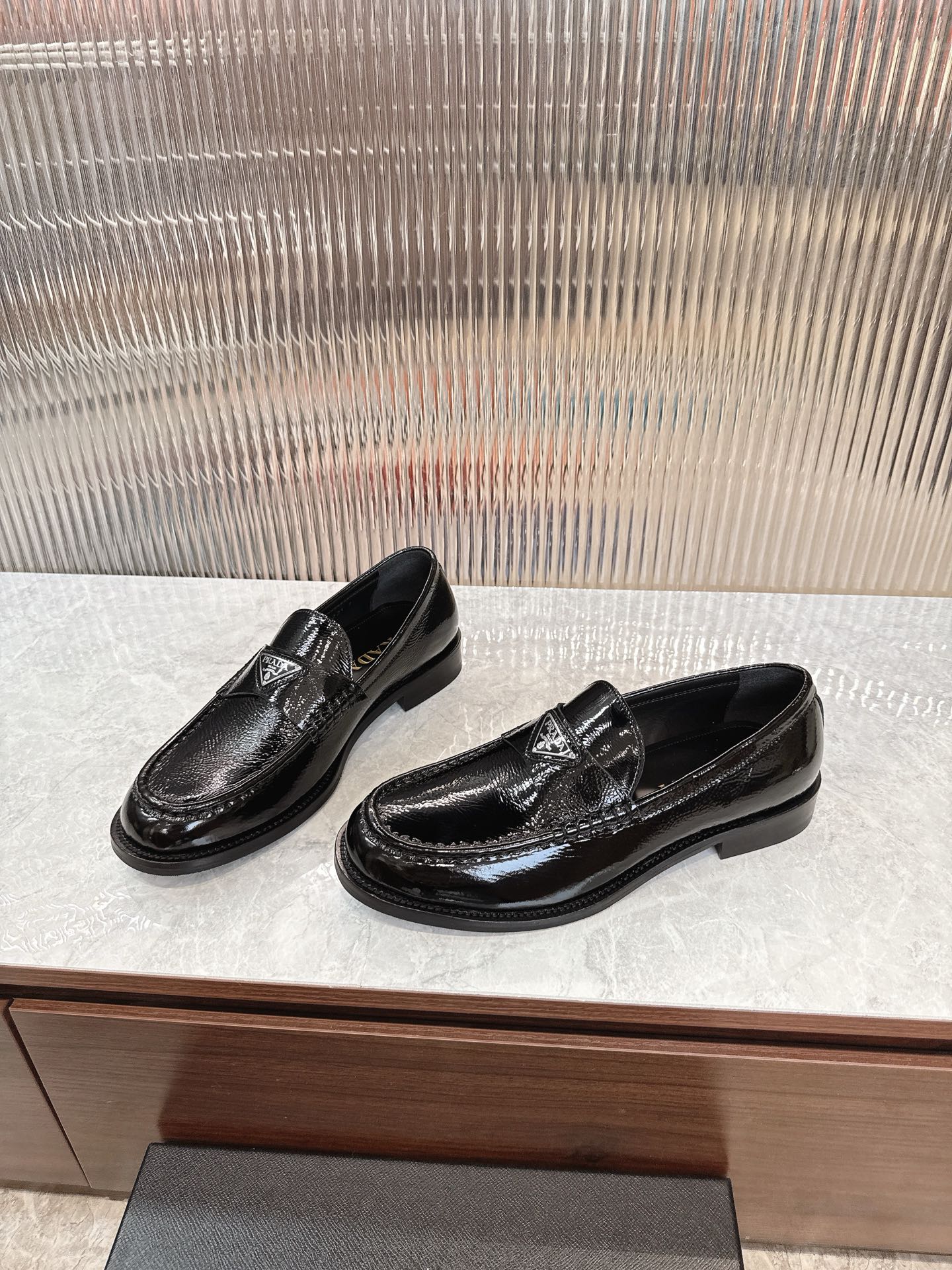 Black slip-on loafers with textured vamp and Prada crest, three-quarter view.
