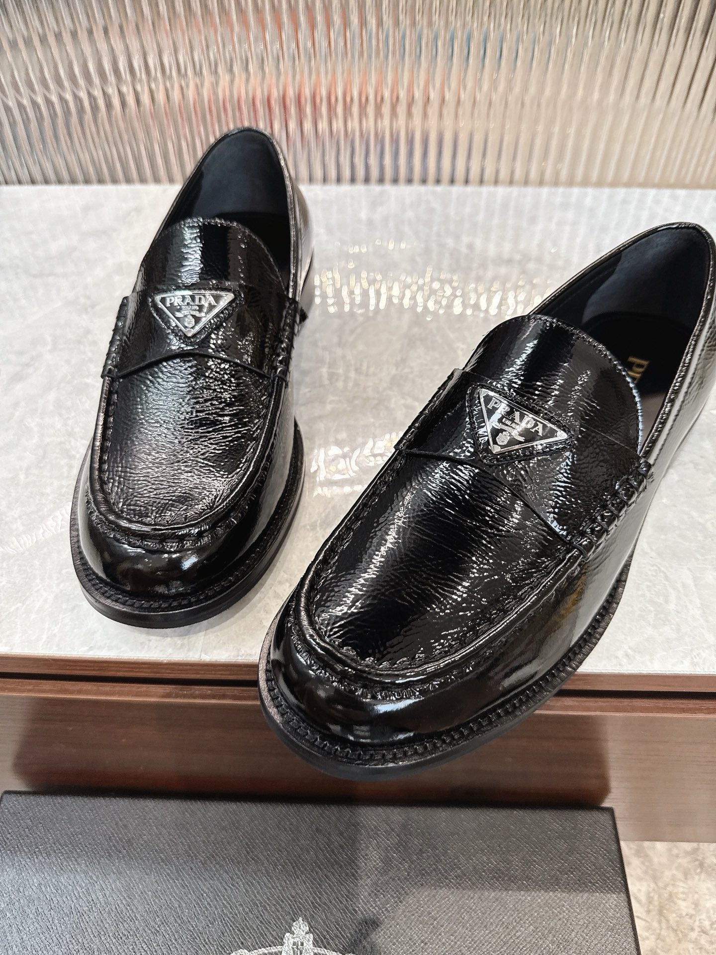 Black shiny loafers with Prada triangle emblem on the upper, close-up view.