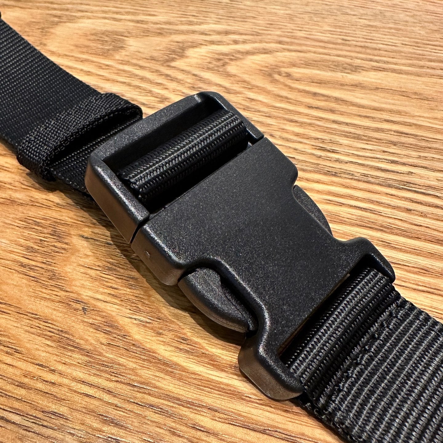 Black adjustable strap with plastic buckle hardware on a crossbody bag.