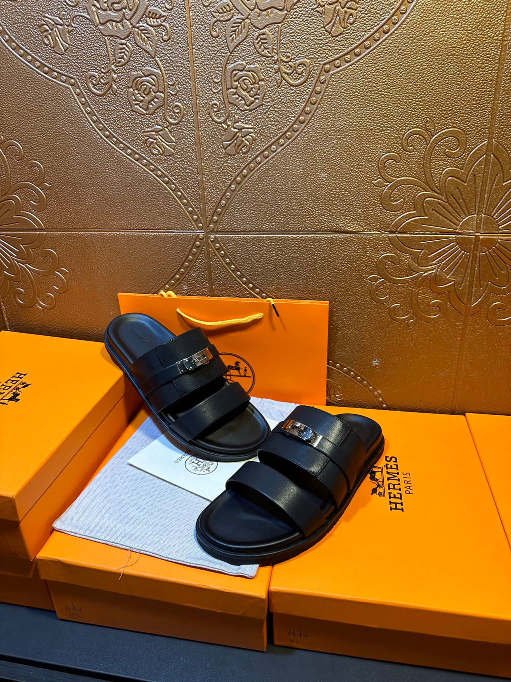 Hermes leather slide sandals on box, dark navy straps with gold-tone buckle detail