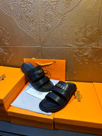 Hermes leather slide sandals on box, dark navy straps with gold-tone buckle detail
