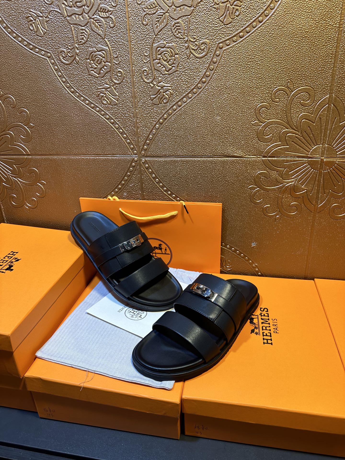 Hermes leather slide sandals on box, dark navy straps with gold-tone buckle detail