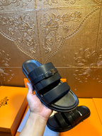 Hermes leather slide sandals held in hand, dark navy straps with gold-tone buckle
