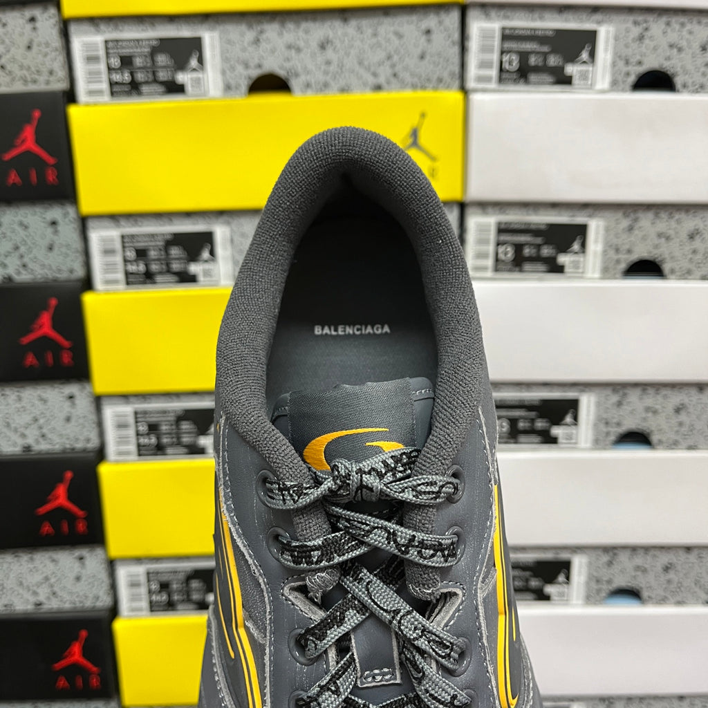 Grey sneaker tongue and lace-up front with small yellow accent and Balenciaga branding.