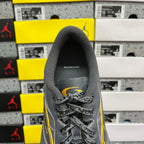 Grey sneaker tongue and lace-up front with small yellow accent and Balenciaga branding.