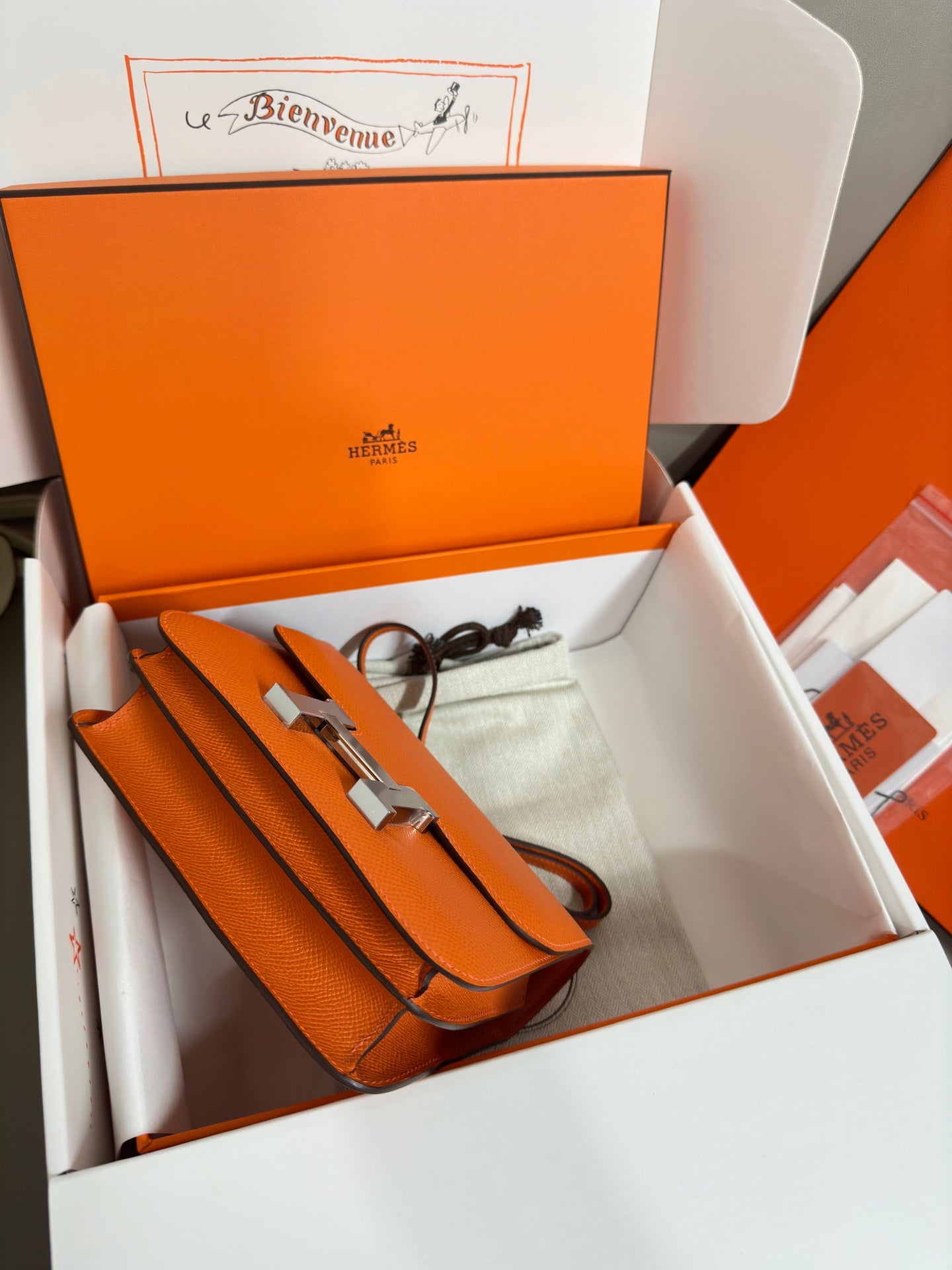 Orange leather bag with long strap and hardware, laid in gift box