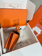 Orange leather bag with strap and front H clasp, partially shown from side
