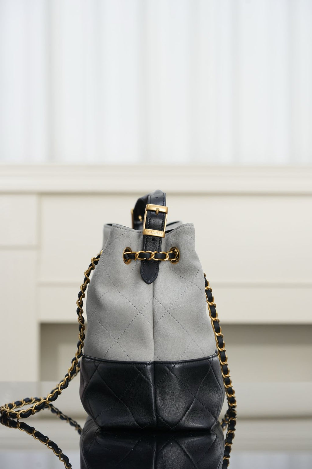 Chanel handbag close-up, top handle and gold chain strap over light gray and black panels