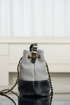 Chanel handbag close-up, top handle and gold chain strap over light gray and black panels