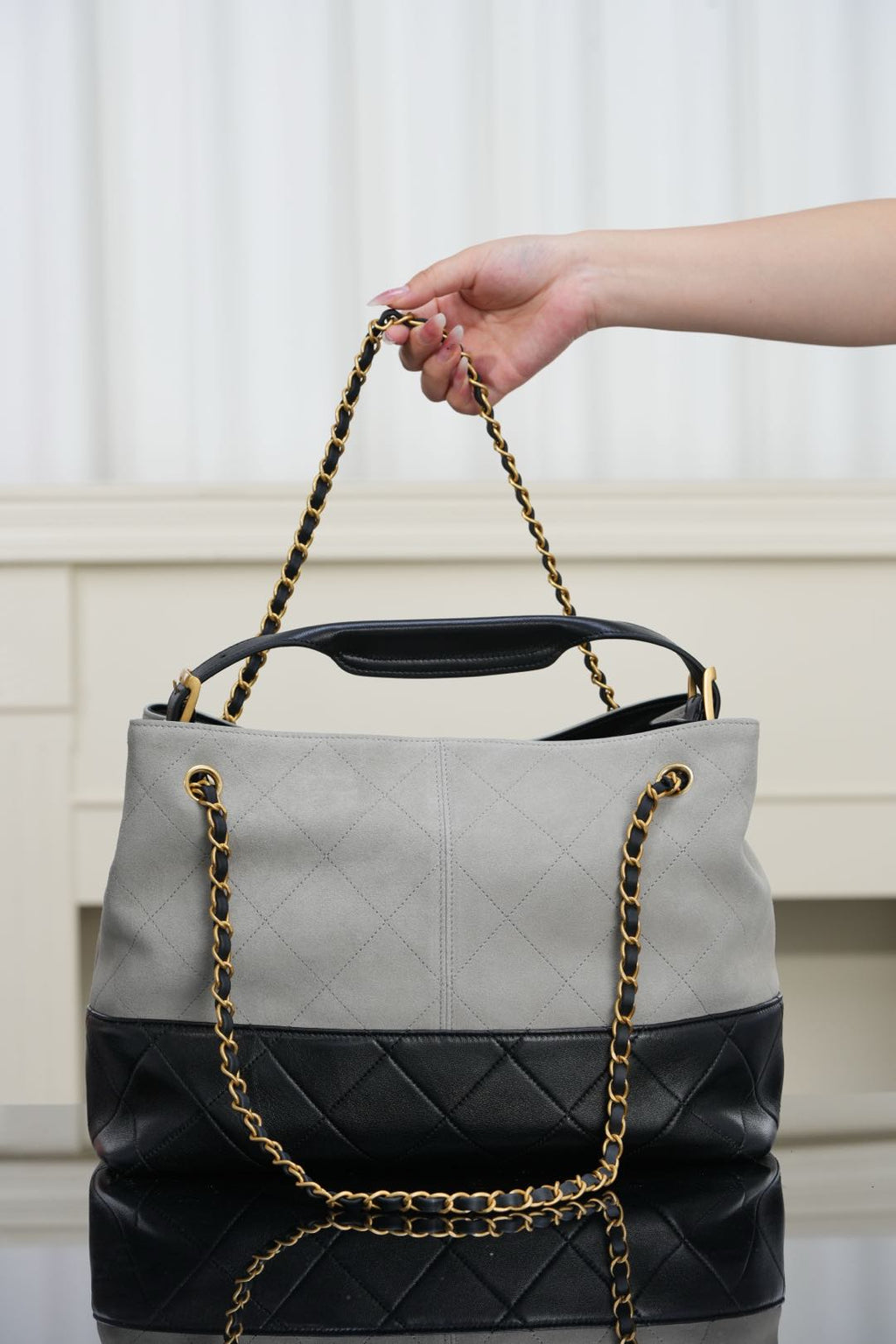 Chanel quilted handbag held by chain strap, light gray body with black bottom panel