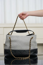 Chanel quilted handbag held by chain strap, light gray body with black bottom panel
