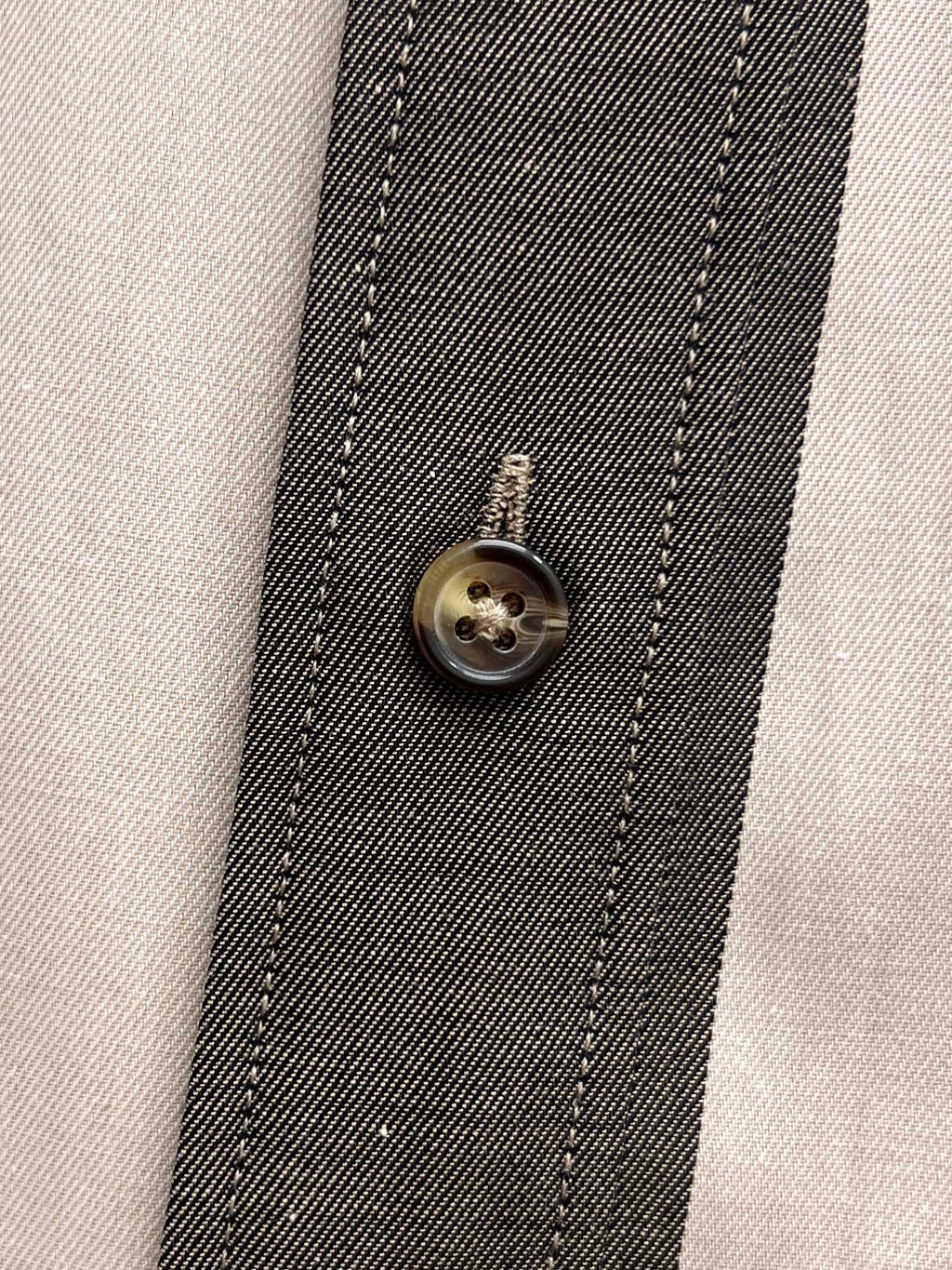 Shirt placket close-up with round metal button and stitched trim in plaid