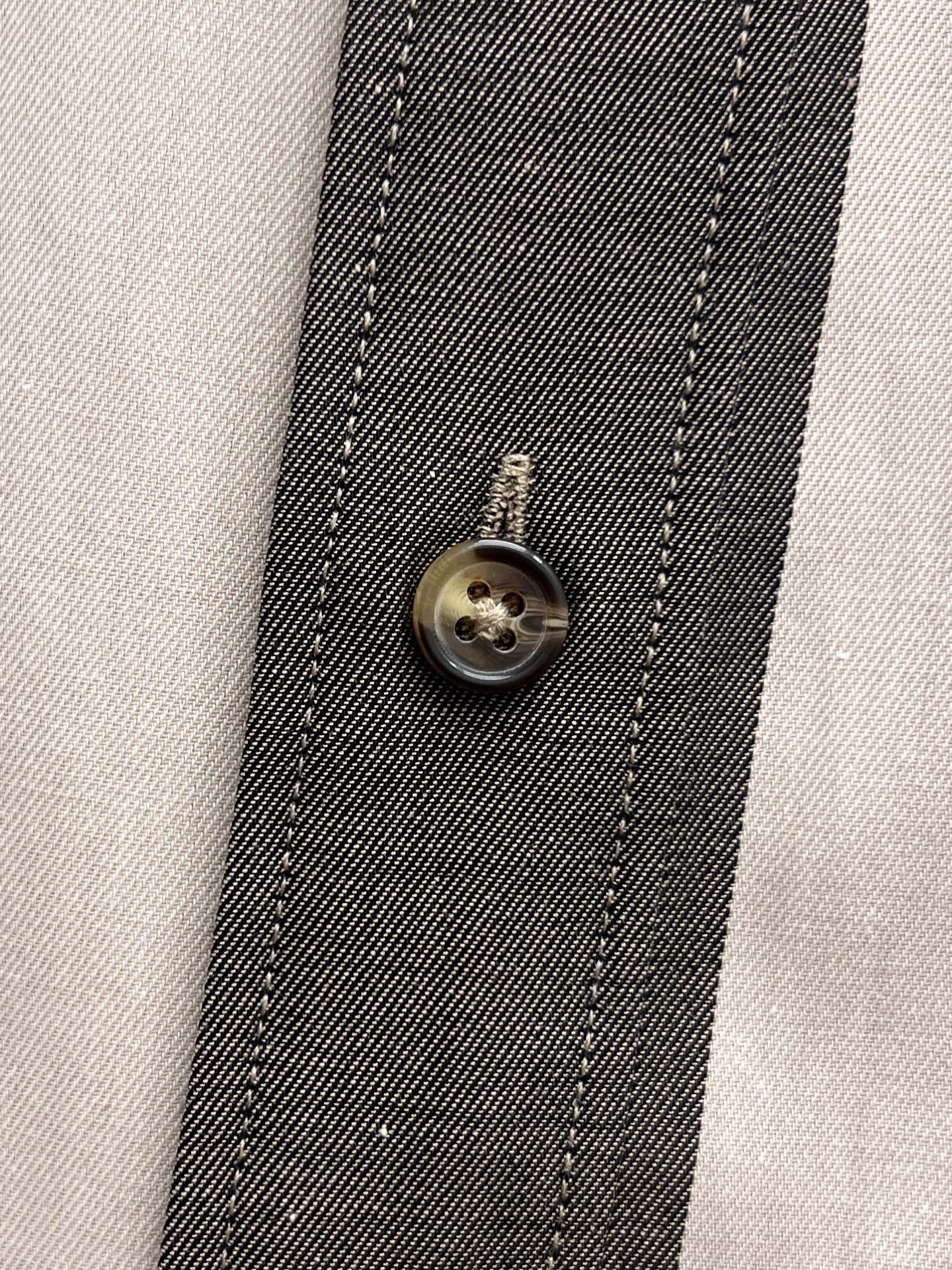 Shirt placket close-up with round metal button and stitched trim in plaid