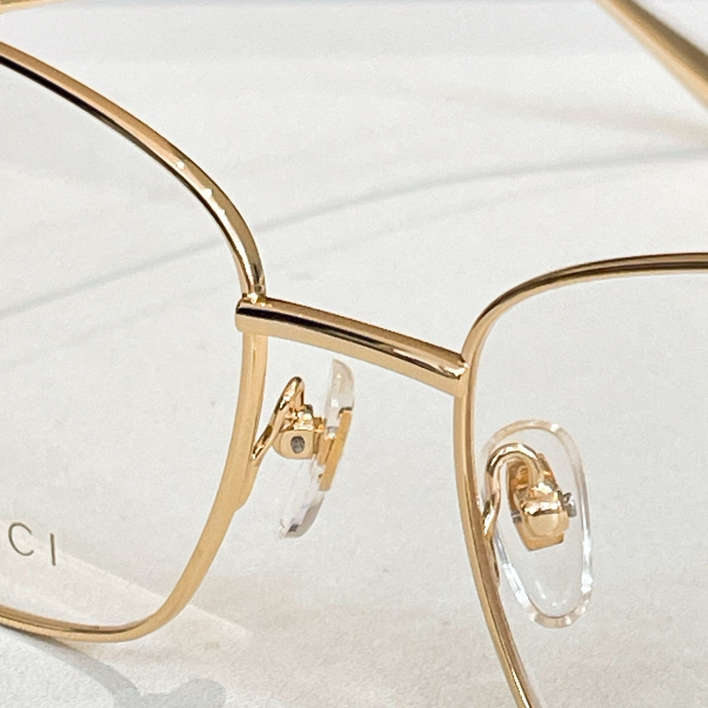 Gucci eyeglass frame in gold metal with clear lens and hinge detail.