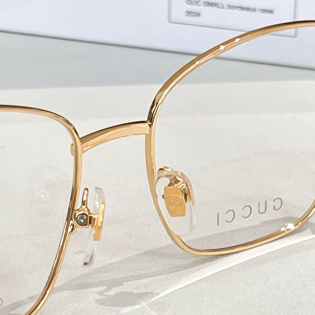 Gucci eyeglass frame in gold metal with side logo plaque and clear lens.