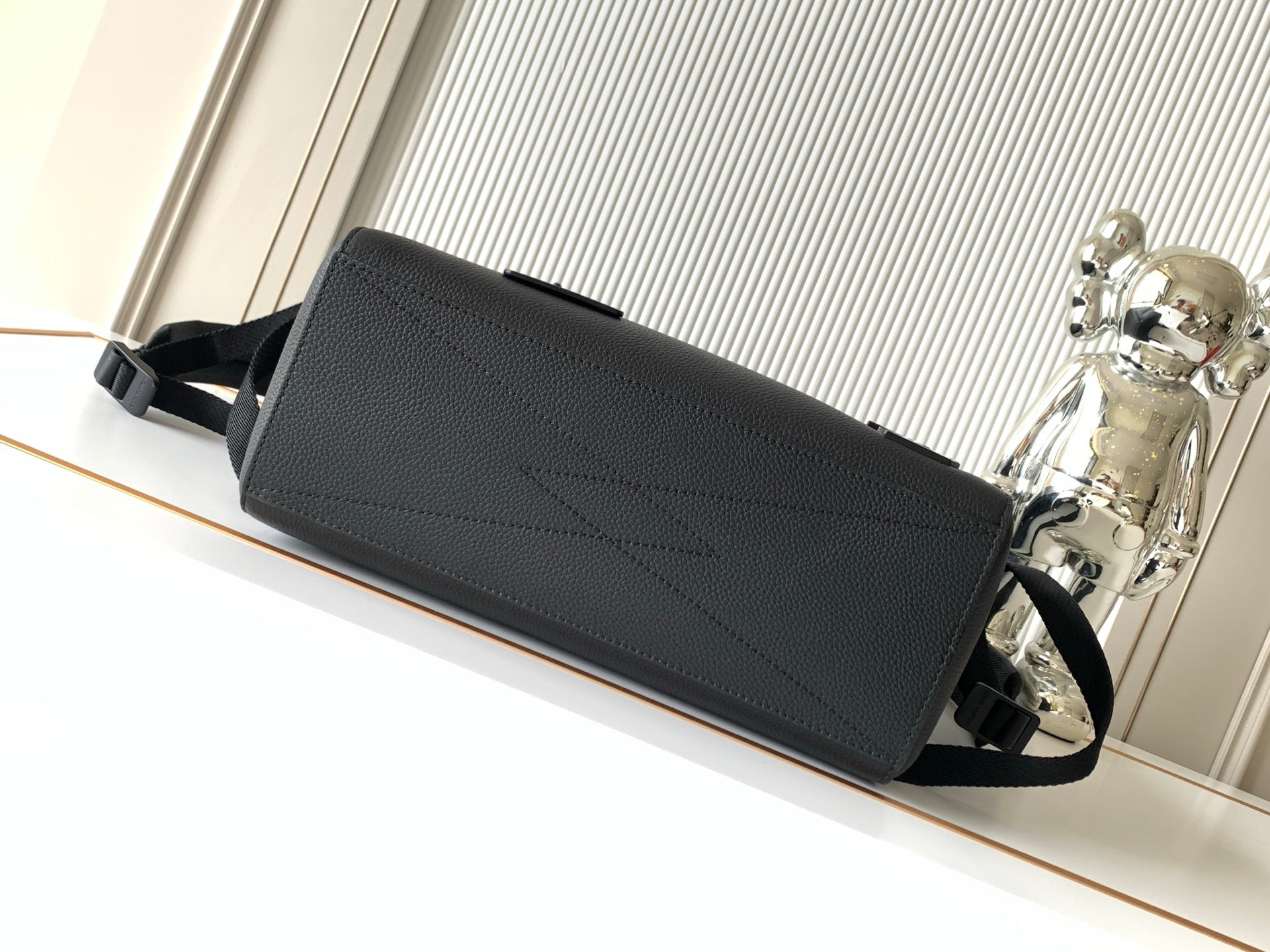 Men's Louis Vuitton bag with front flap and top handle, dark leather-look texture.
