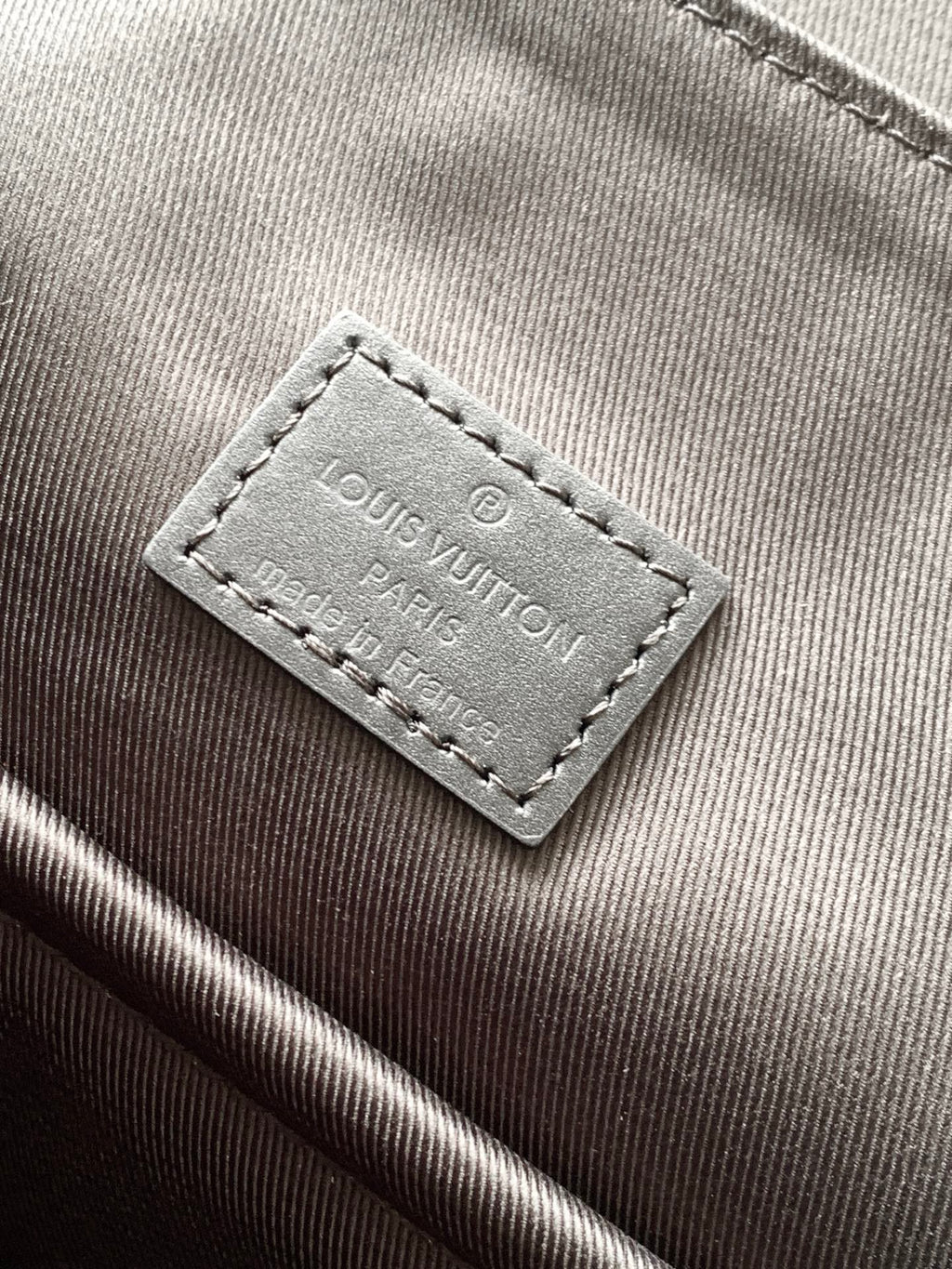 Men's Louis Vuitton bag close-up of interior brand label on dark fabric lining.