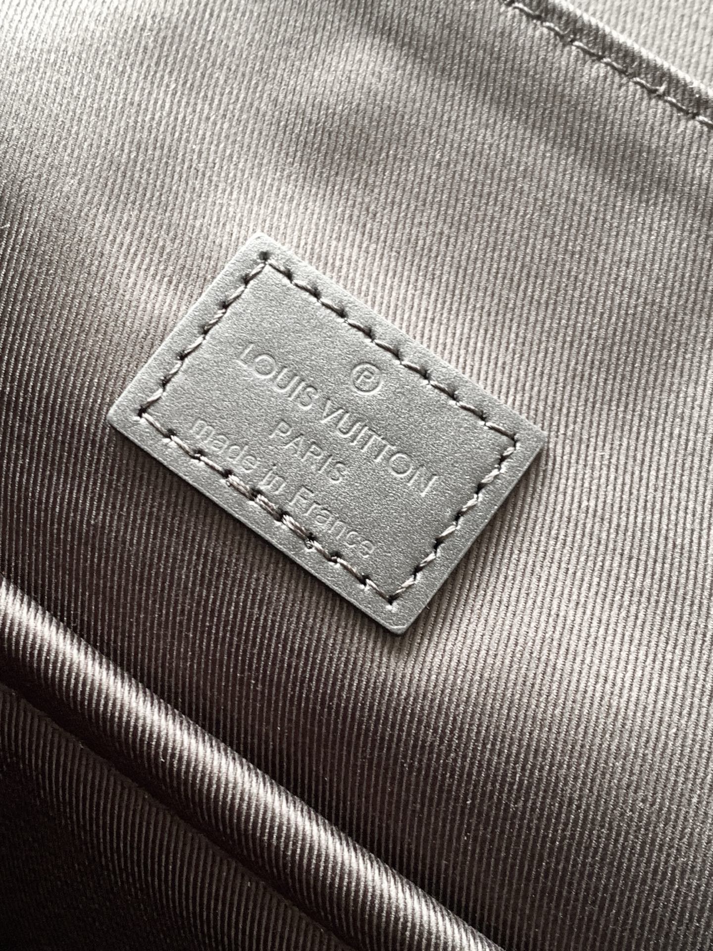 Men's Louis Vuitton bag close-up of interior brand label on dark fabric lining.