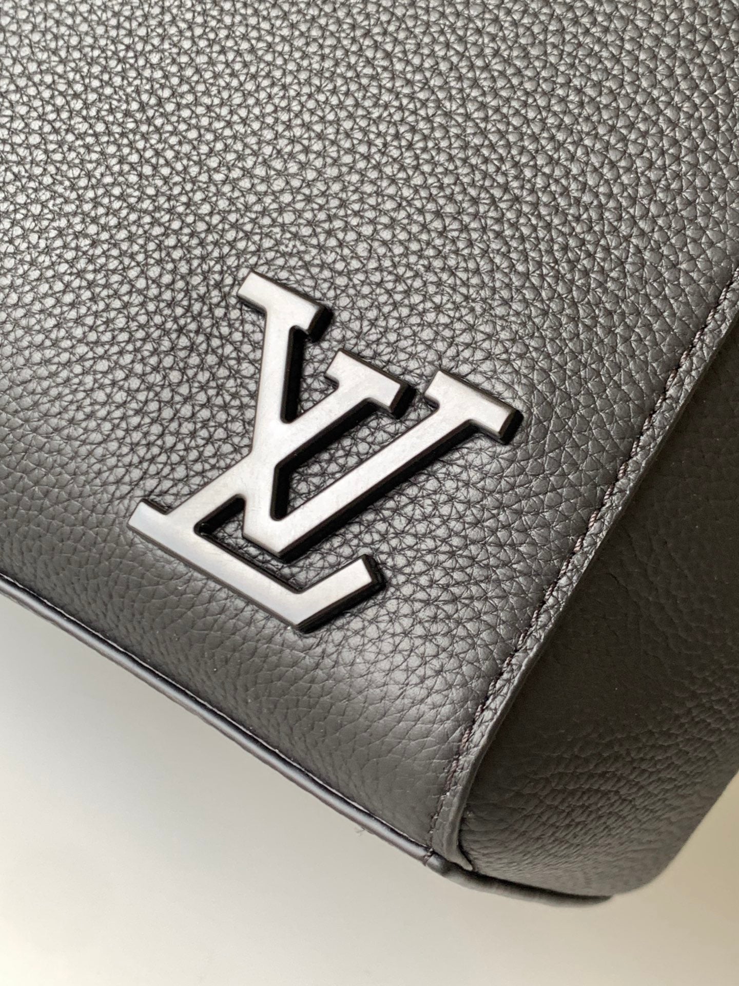 Men's Louis Vuitton bag close-up of metal logo on dark grained leather-look.